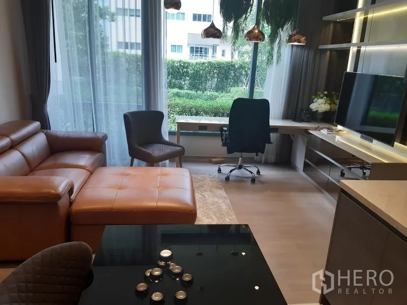 Condominium for rent or sale in Watthana, Bangkok - Bright living room with leather sofa, floor-to-ceiling windows, garden view, TV wall and work desk at a Sukhumvit condo.