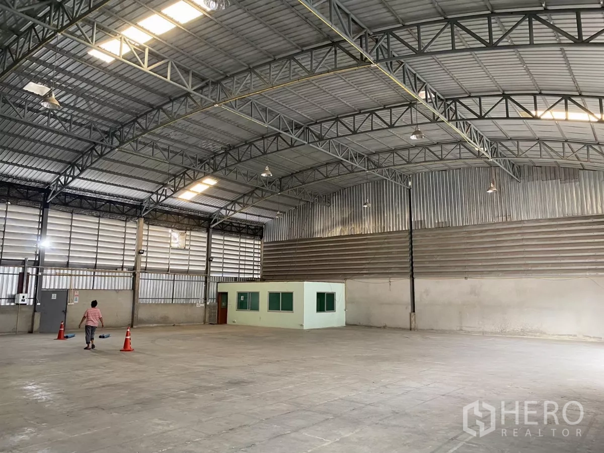 Warehouse for rent - Spacious warehouse interior with high steel truss roof, skylights, concrete floor, and a small office room.