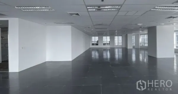 Office Space for rent - Spacious office floor with white columns, suspended ceiling lighting, and rows of windows for natural light.