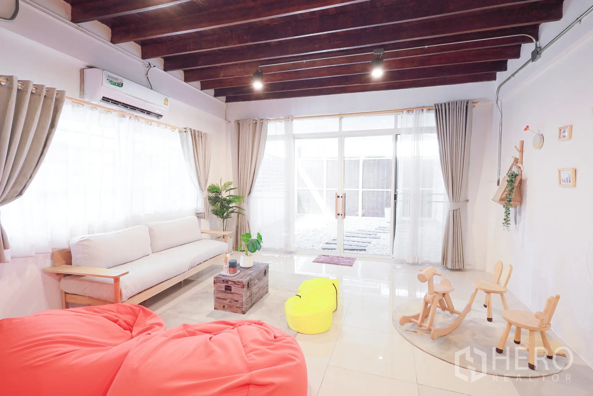 Townhouse for rent in Din Daeng, Bangkok - Living room with sofa and sliding glass doors opening to a pebble courtyard and kids’ play corner.