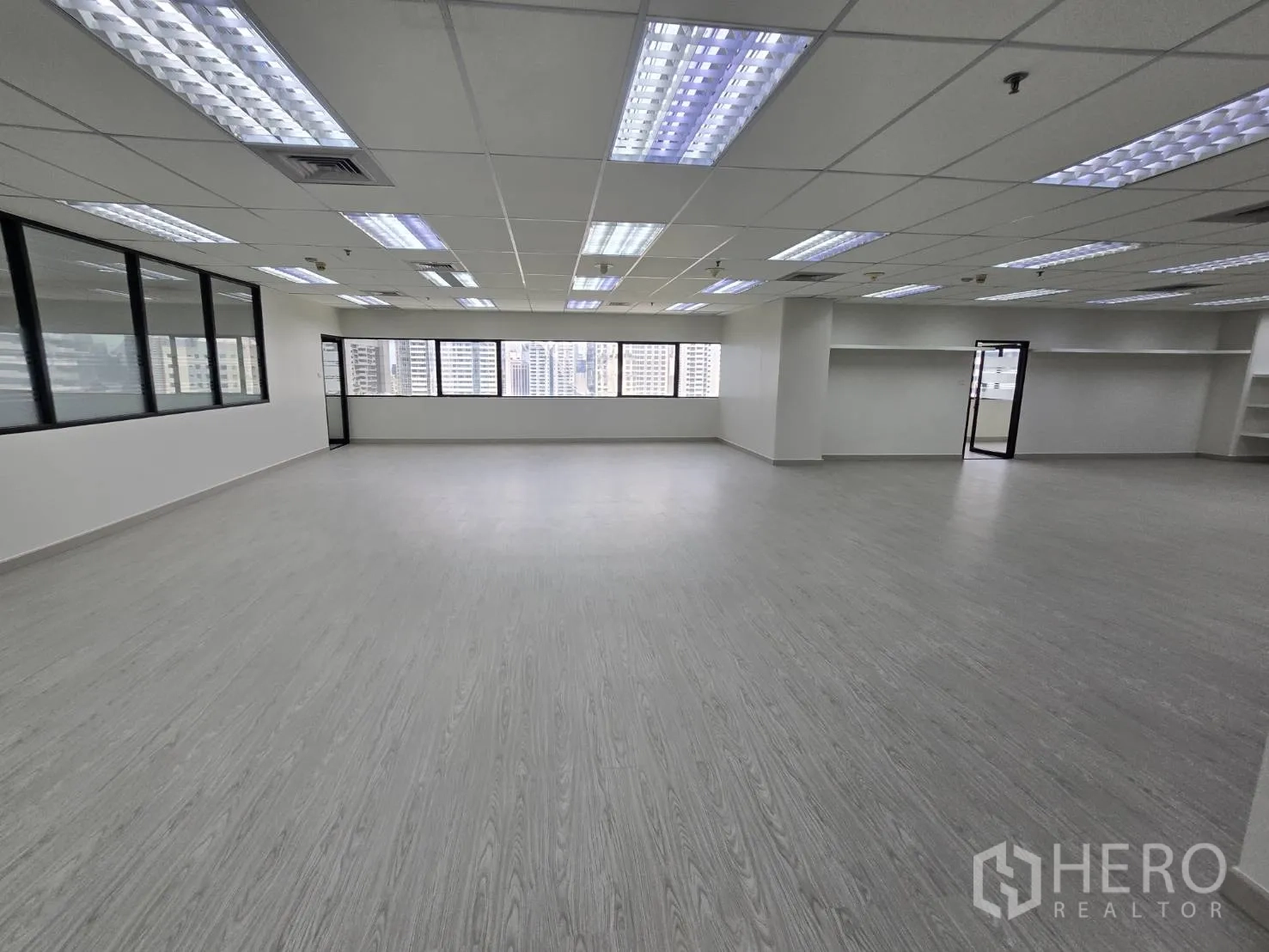 Office Space for rent in Khlong Toei, Bangkok - Corner office area with broad windows, city skyline views, and grid ceiling lights.