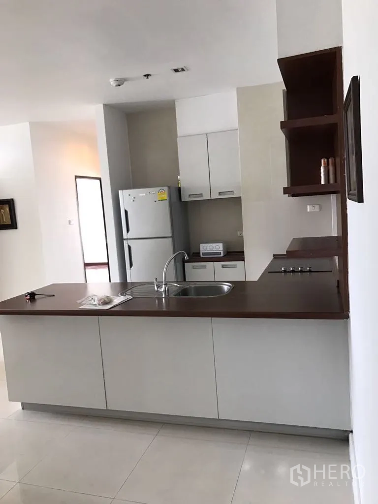 Condominium for rent in Watthana, Bangkok - Watthana Bangkok condo kitchen with island sink, wood countertop, cooktop and white cabinetry beside a full-size fridge.