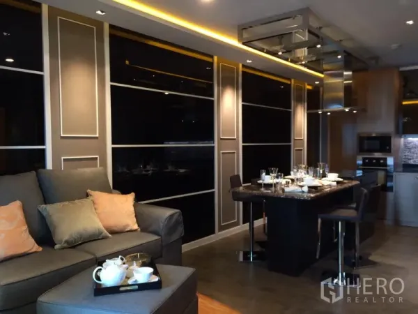 Condominium for rent in Ratchathewi, Bangkok - Open-plan living and dining with dark feature panels and warm recessed lighting.