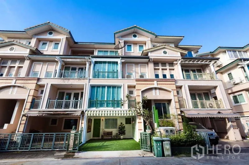 联排别墅 出租在Lat Phrao, Bangkok - 四层联排别墅外观，带多处阳台、绿色围栏与条纹遮阳篷，街景清静。