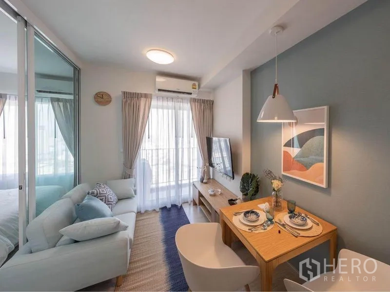 Condominium for sale in Huai Khwang, Bangkok - Bright living and dining area in a modern 1-bedroom condo with sofa, TV, and sliding door to a small balcony.