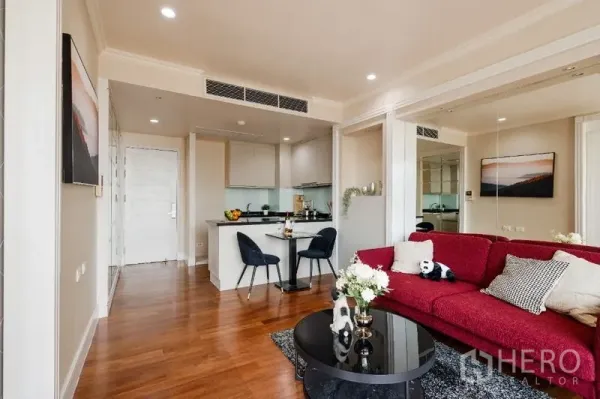 คอนโด ขาย - ห้องนั่งเล่นสว่าง โซฟาสีแดง ครัวเปิด และพื้นไม้ในคอนโดสุขุมวิท