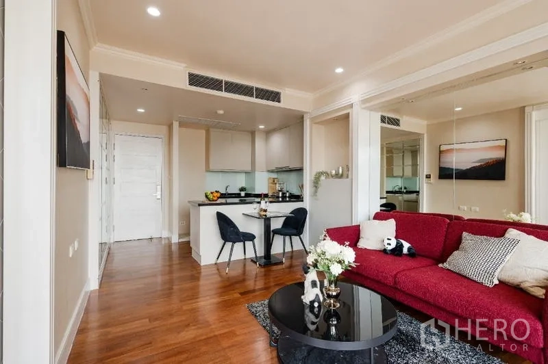 คอนโด ขาย - ห้องนั่งเล่นสว่าง โซฟาสีแดง ครัวเปิด และพื้นไม้ในคอนโดสุขุมวิท