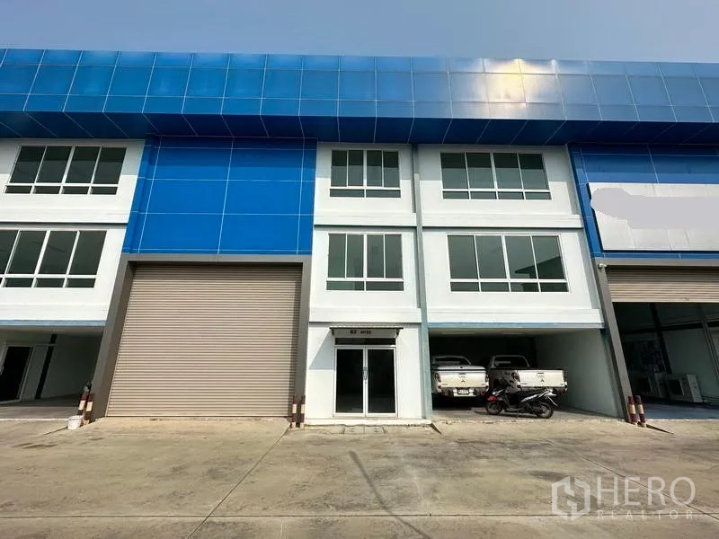货栈 出租在Bang Phli, Samut Prakan - 园区内现代仓库外观，蓝色立面，大卷闸门与玻璃办公室入口。