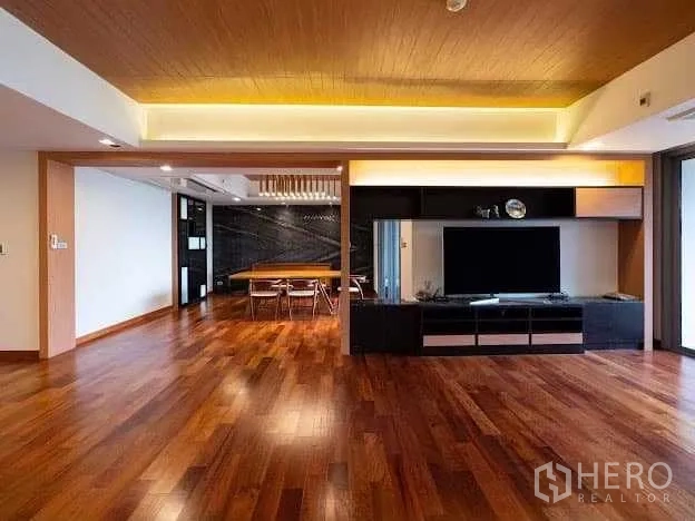 Condominium for sale in Yan Nawa, Bangkok - Open‑plan lounge with TV unit facing the dining area, warm cove lighting and timber flooring.
