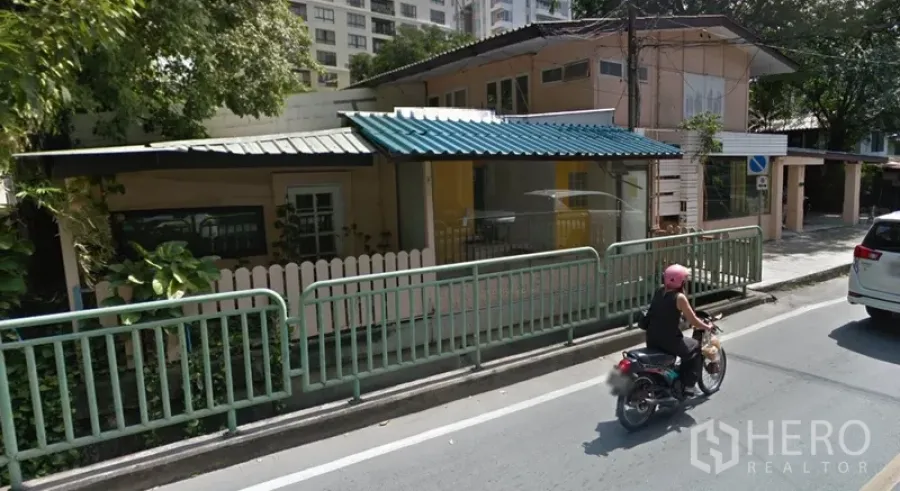 พื้นที่ขายปลีก ให้เช่าในWatthana, Bangkok - อาคารเชิงพาณิชย์สองชั้นติดถนน หน้ากระจก พร้อมกันสาดโลหะและรั้วข้างทาง ใต้ร่มเงาต้นไม้