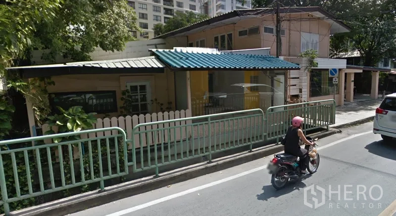 พื้นที่ขายปลีก ให้เช่าในWatthana, Bangkok - อาคารเชิงพาณิชย์สองชั้นติดถนน หน้ากระจก พร้อมกันสาดโลหะและรั้วข้างทาง ใต้ร่มเงาต้นไม้