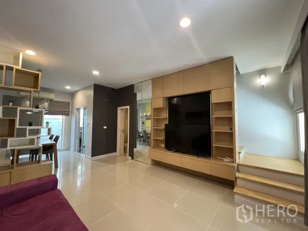 Townhouse for rent in Wang Thonglang, Bangkok - Lounge with large media unit, glossy tiles and stairs to upper floor.