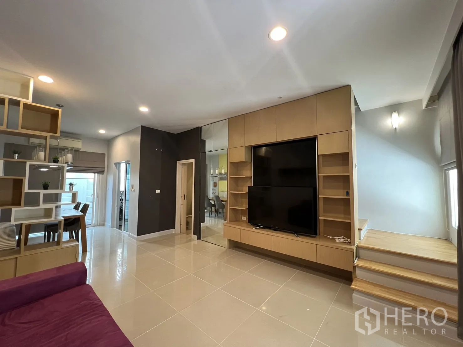 Townhouse for rent in Wang Thonglang, Bangkok - Lounge with large media unit, glossy tiles and stairs to upper floor.