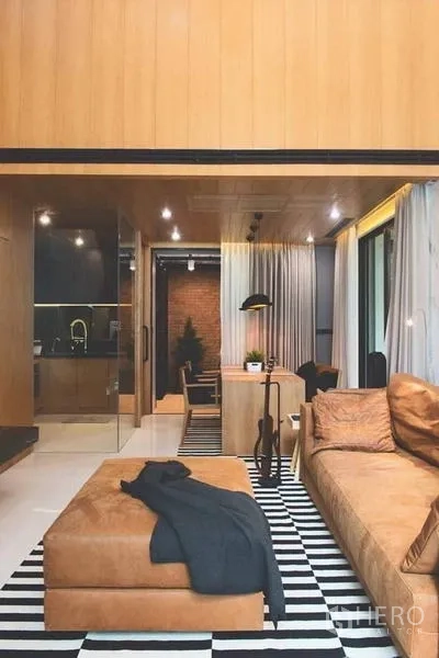 Townhouse for sale in Lak Si, Bangkok - Double-height living room with leather sofa, striped rug, and feature staircase.