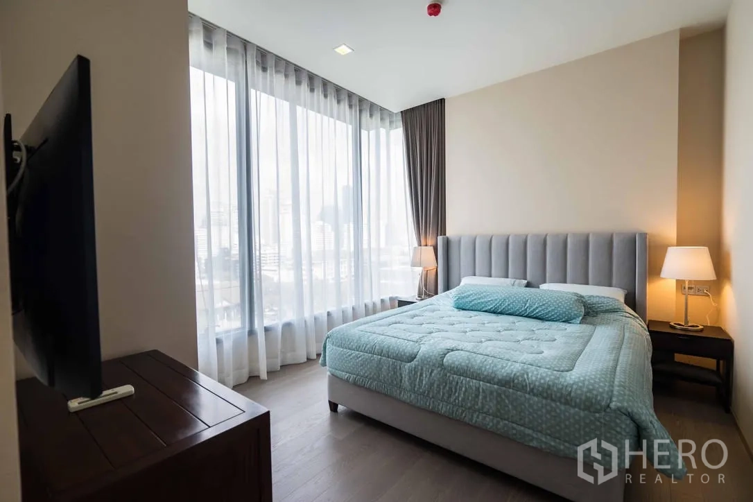 Condominium for rent in Watthana, Bangkok - Master bedroom with upholstered bed, bedside lamps and wraparound skyline windows.