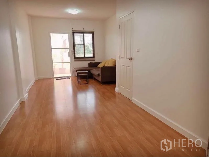 Townhouse for rent in Suan Luang, Bangkok - Long living area with wood floors, sofa by the window and door to outside
