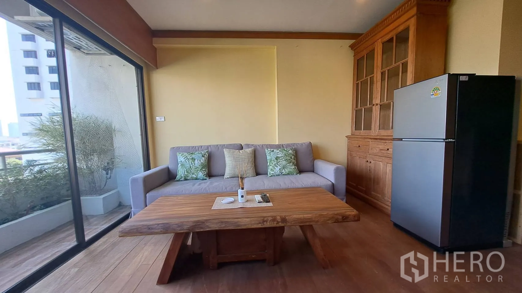 Condominium for rent in Khlong Toei, Bangkok - Sofa corner by the balcony with wooden coffee table and tall cabinet.