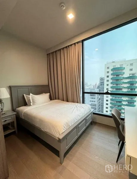 Condominium for rent in Watthana, Bangkok - Guest bedroom with double bed, desk, and large window overlooking neighboring towers.