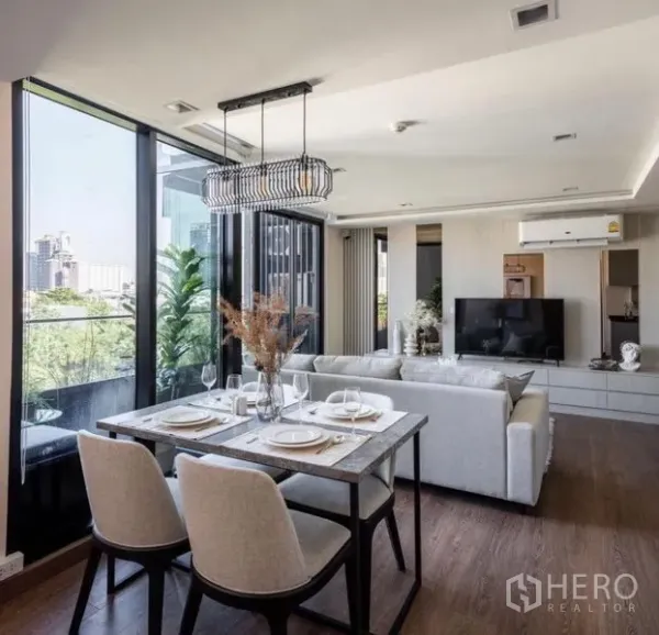 Condominium for rent or sale in Phra Khanong, Bangkok - Open-plan dining and living area with modern chandelier, glass walls and greenery outside.