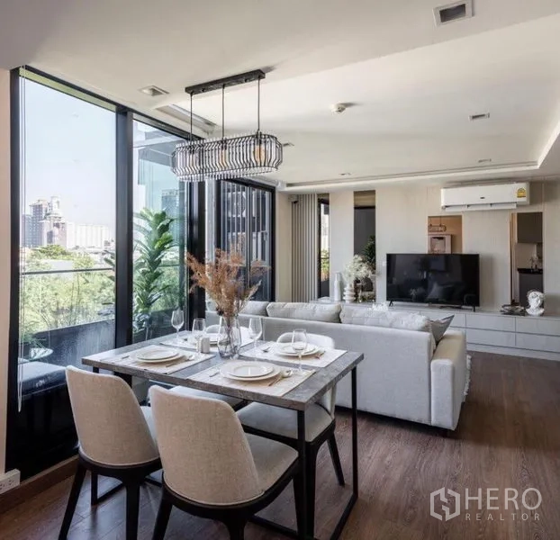 Condominium for rent or sale in Phra Khanong, Bangkok - Open-plan dining and living area with modern chandelier, glass walls and greenery outside.
