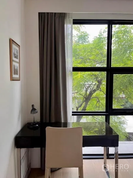Condominium for rent in Watthana, Bangkok - Workstation nook with black desk and chair beside a full-height window and tree views.