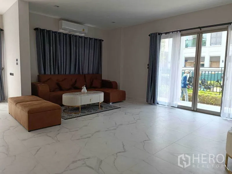 Detached House for rent in Bueng Kum, Bangkok - Ground-floor lounge with marble-look tiles, sectional sofa, and sliding glass doors to the garden.