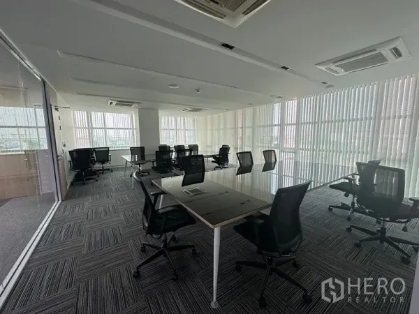 Office Space for rent - Open-plan workspace with multiple desks, carpet tiles and floor-to-ceiling windows with vertical blinds.
