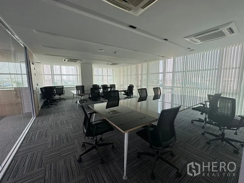 Office Space for rent - Open-plan workspace with multiple desks, carpet tiles and floor-to-ceiling windows with vertical blinds.