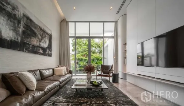 Detached House for sale in Saphan Sung, Bangkok - Bright living room with floor-to-ceiling windows, leather sofa and garden view.