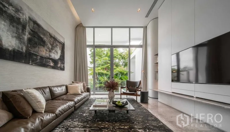 Detached House for sale in Saphan Sung, Bangkok - Bright living room with floor-to-ceiling windows, leather sofa and garden view.