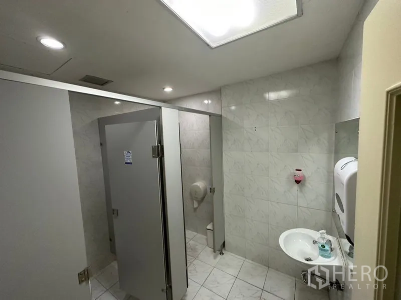 Office Space for rent in Khlong Toei, Bangkok - Clean tiled restroom with stalls, sink and overhead lighting inside the office.