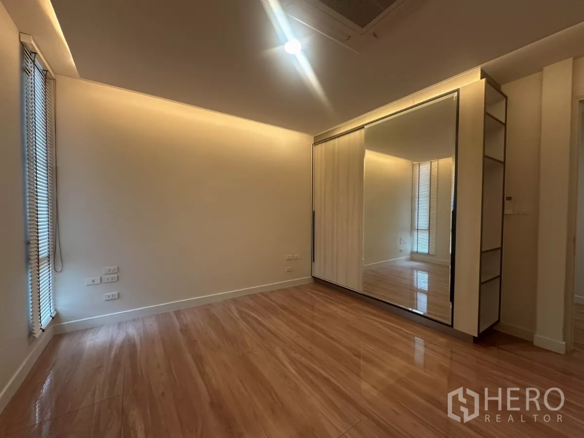 Townhouse for rent in Watthana, Bangkok - Bedroom with wood floors and mirrored sliding wardrobe with ambient lighting.