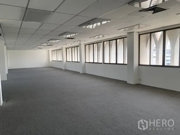 Office Space for rent in Bang Kapi, Bangkok - Long open workspace featuring carpeted floors, acoustic grid ceiling panels, and arched-frame windows along the facade.