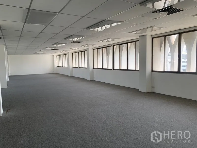 Office Space for rent in Bang Kapi, Bangkok - Long open workspace featuring carpeted floors, acoustic grid ceiling panels, and arched-frame windows along the facade.