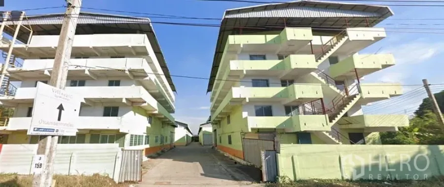 คลังสินค้า ให้เช่าในNonthaburi - มุมมองจากถนนสู่ทางเข้าโครงการโกดัง อาคารหลายชั้นคู่พร้อมบันไดภายนอกและถนนกลาง บางกรวย นนทบุรี