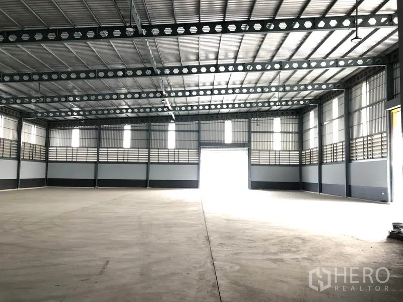 工厂 出租在Bang Len, Nakhon Pathom - 宽敞的仓库内部，高钢梁屋顶与卷闸门入口。