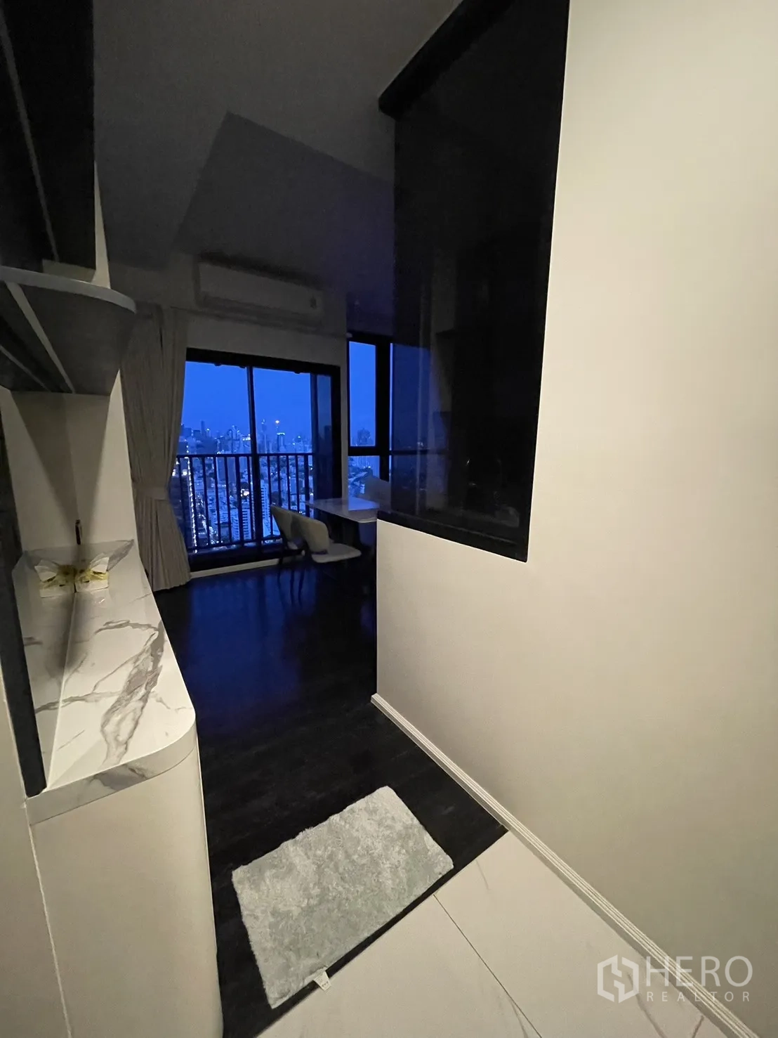 Condominium for rent in Watthana, Bangkok - Hallway opening to the living room with city skyline visible through windows.