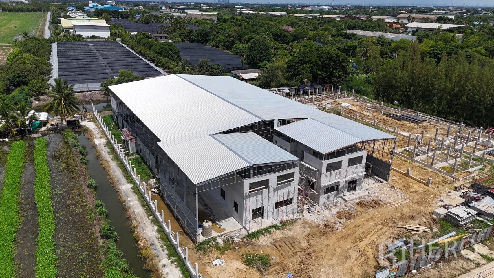 Factory for rent in Phutthamonthon, Nakhon Pathom - Front aerial of factory complex with metal roofs, scaffolding, and yard space.