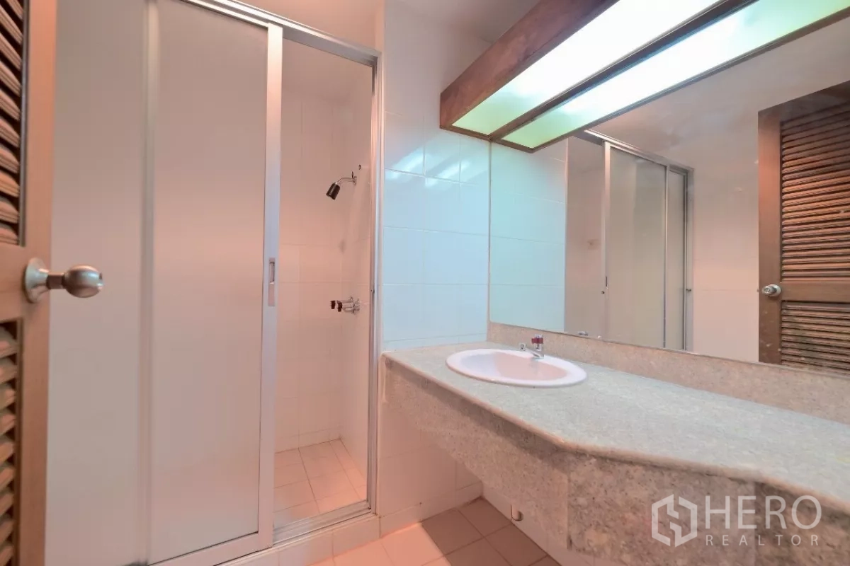 Townhouse for sale in Watthana, Bangkok - Bathroom with long stone vanity, large mirror, and a glass-door shower stall.
