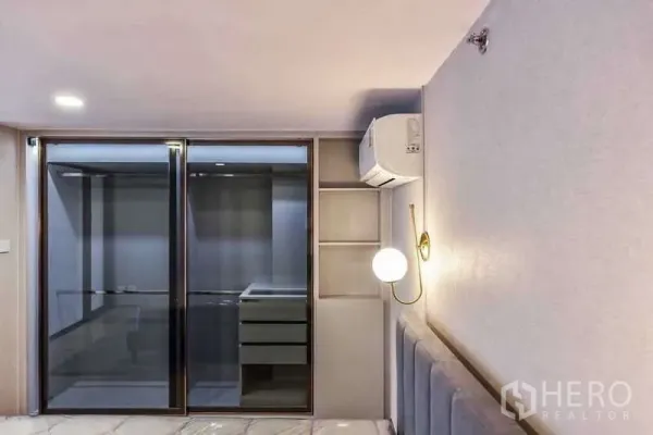 Condominium for rent in Huai Khwang, Bangkok - Bedroom wall with glass wardrobe, built-in shelves and sconce lighting.