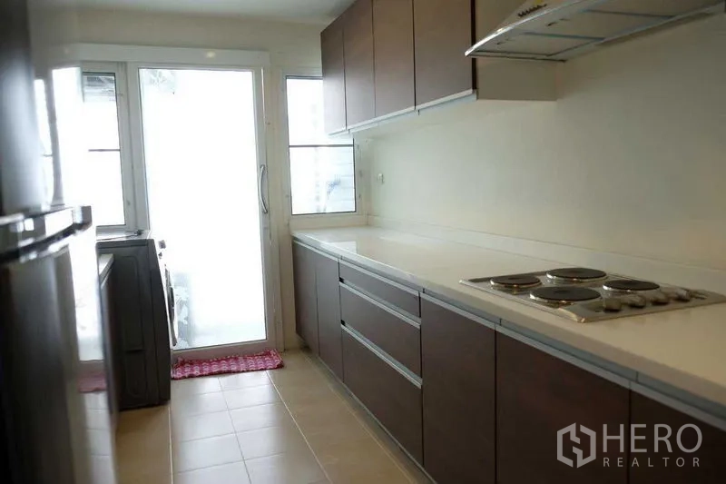 คอนโด ขายในKhlong San, Bangkok - ครัวปิดแบบแกลเลย์ เคาน์เตอร์ยาว ตู้ล่าง-บนสีเข้ม เตาไฟฟ้า และประตูกระจกออกระเบียง.