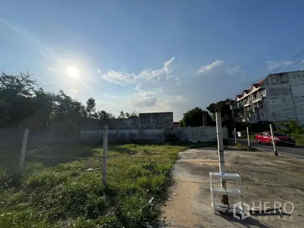 ที่ดิน ขายในBang Na, Bangkok - ที่ดินเปิดโล่งข้างถนนซอย มีอาคารพักอาศัยเตี้ยและรถสีแดงใกล้แนวรั้ว