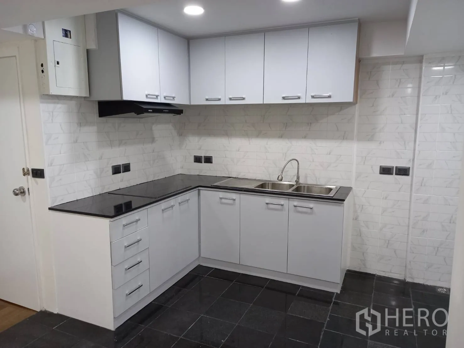 公寓 出租在Khlong Toei, Bangkok - L形厨房，白色橱柜、黑色台面、抽油烟机与双槽水槽。