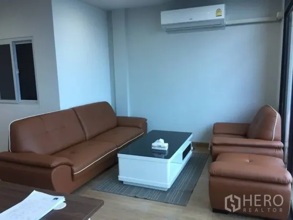 Home Office for rent or sale in Prawet, Bangkok - Furnished lounge with brown leather sofa set, white coffee table, and wall-mounted air conditioner.