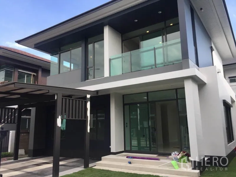 Detached House for rent in Bang Kapi, Bangkok - Angle view of the house showing clear glass balcony, large windows and a neat front lawn.