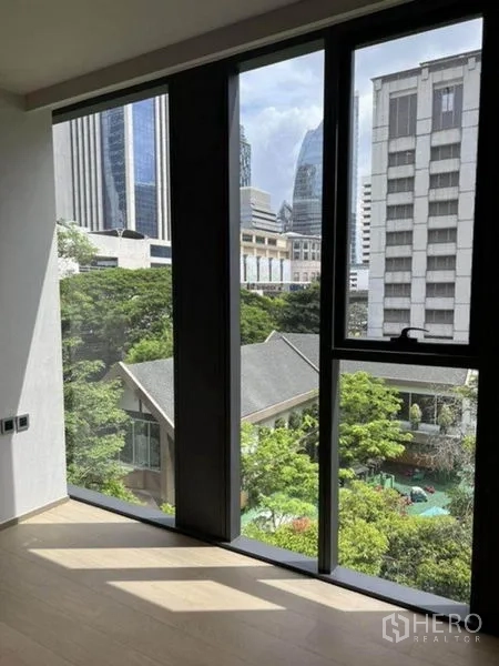 Condominium for rent in Pathum Wan, Bangkok - Bedroom with tall windows overlooking greenery and Bangkok skyline.