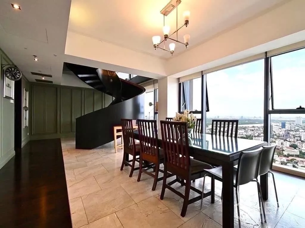 Condominium for rent in Sathon, Bangkok - Dining area with eight-seat table, floor-to-ceiling windows and a bold black spiral staircase.