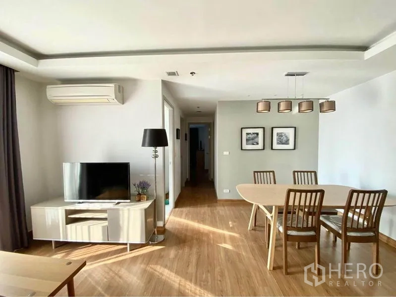 Condominium for rent in Huai Khwang, Bangkok - Living room with TV unit, floor lamp and dining set in natural light.