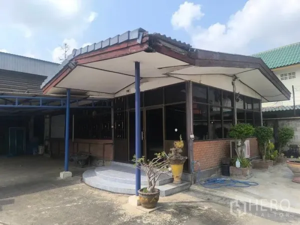 Warehouse for rent in Lat Lum Kaeo, Pathum Thani - Glass-front office pavilion with canopy beside the warehouse entrance, landscaped with potted plants.