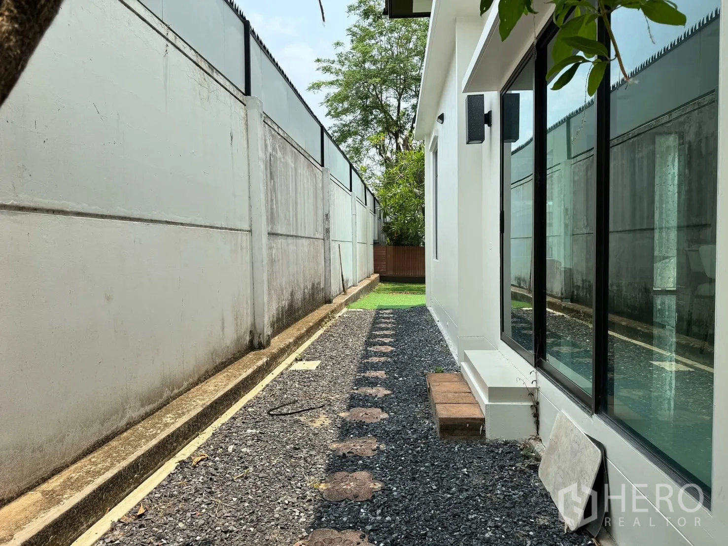 Detached House for rent in Prawet, Bangkok - Side walkway with gravel stepping stones beside the house and windows, leading to a small lawn.